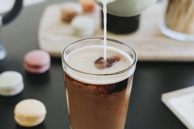 mælk hældes i glas med kaffe fra kaffemaskine